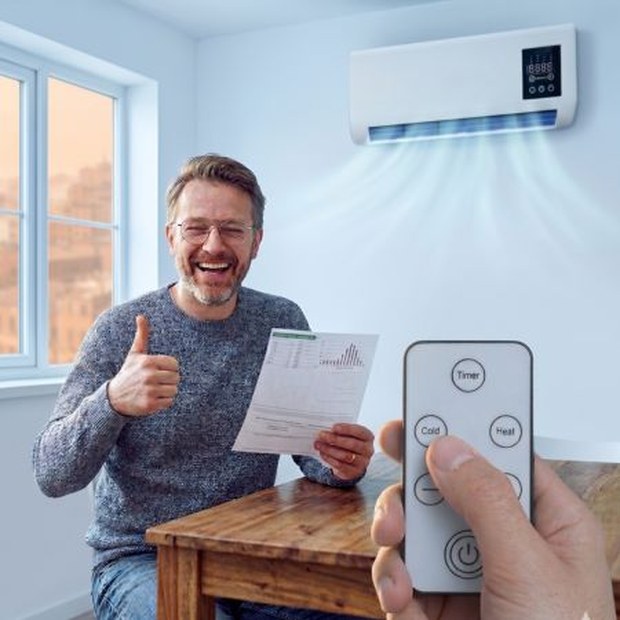 Smiling man pointing the EpiCooler portable AC remote control at the wall-mounted unit blowing cool air in his living room